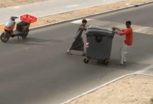 صورة طفل ومقيم يبعدان حاوية عن الطريق في مشهد إنساني بالعين