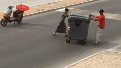 صورة طفل ومقيم يبعدان حاوية عن الطريق في مشهد إنساني بالعين